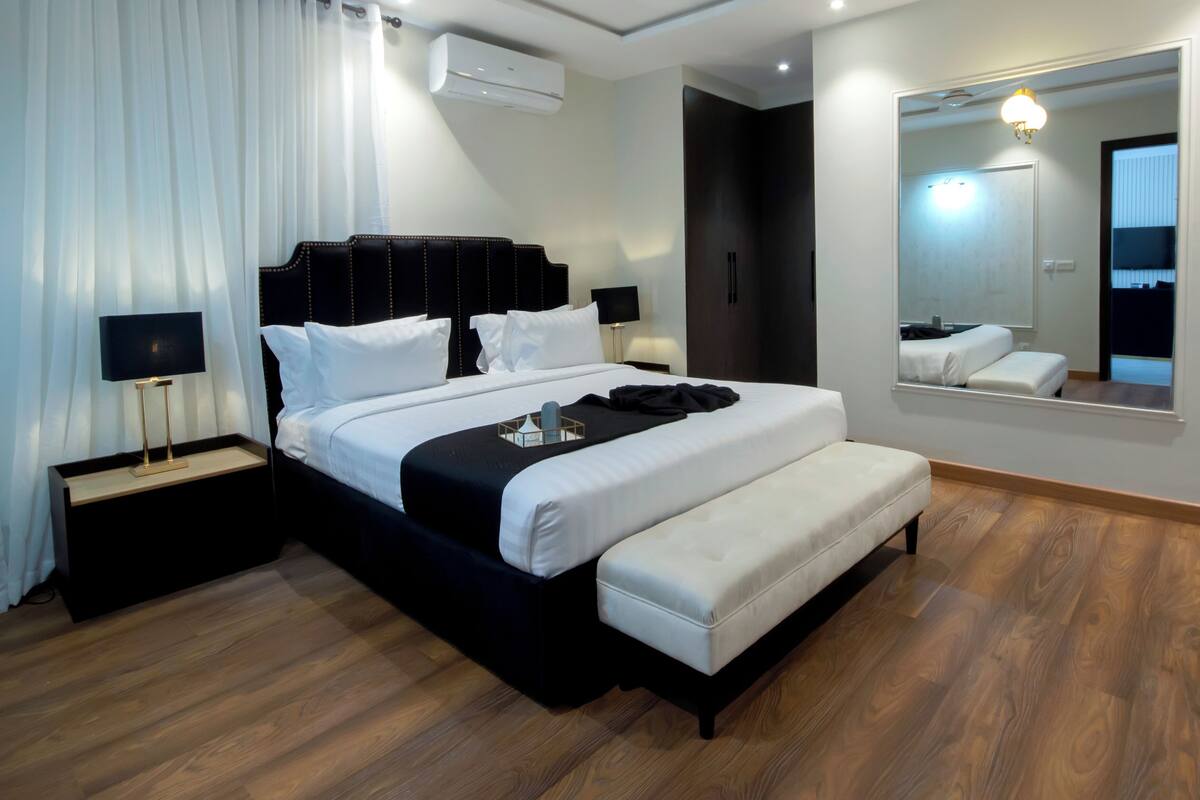 Une chambre d’hôtel moderne avec un grand lit, des tables de chevet, un banc, un miroir et une armoire.