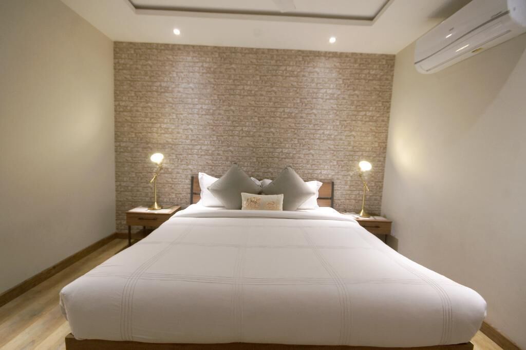 A neatly made bed with a white bedspread and pillows, two bedside lamps, and a brick-patterned wall.