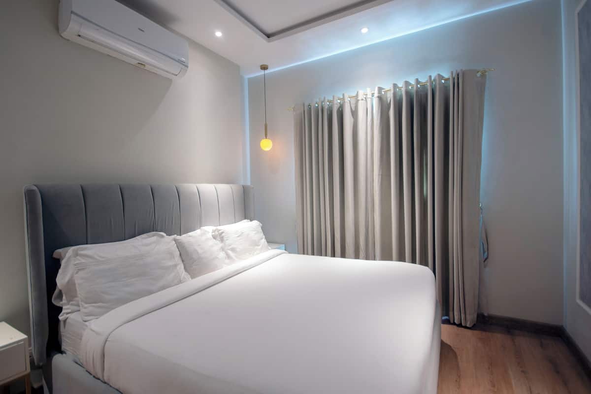 Une chambre d’hôtel moderne équipée d’un grand lit, d’une table de chevet, d’un climatiseur et d’un rideau.
