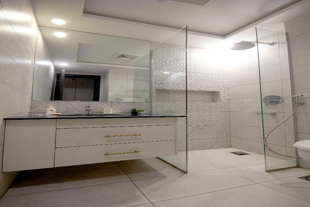 Une salle de bain moderne avec une douche à parois de verre, un meuble-lavabo blanc doté de poignées dorées et un grand miroir.