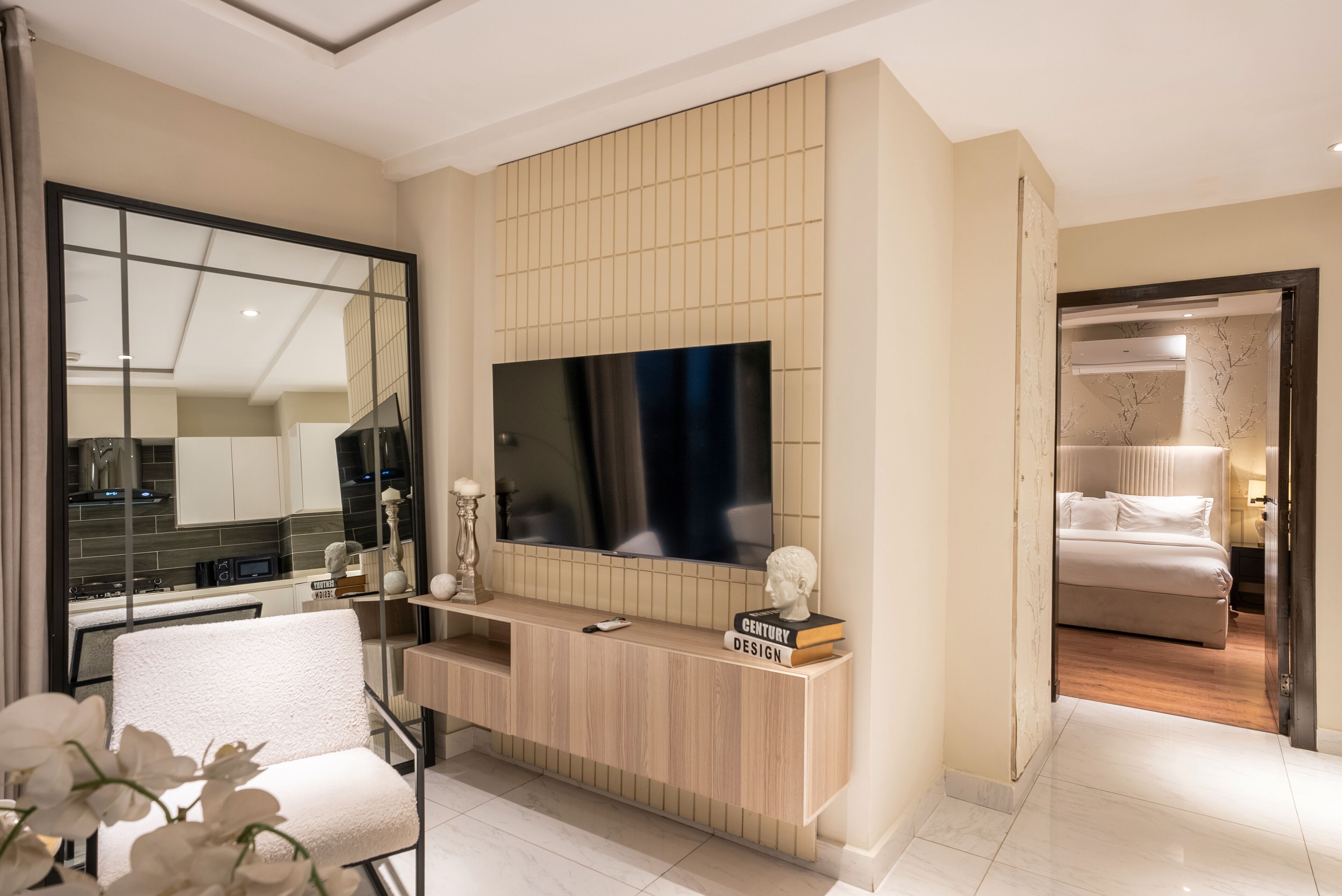 Una sala de estar moderna con un televisor de pantalla plana grande, una consola de madera y un sillón blanco.