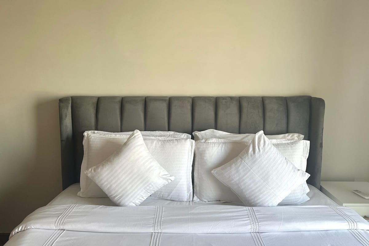 Un lit avec une tête de lit rembourrée de couleur grise, une literie blanche et deux oreillers blancs.