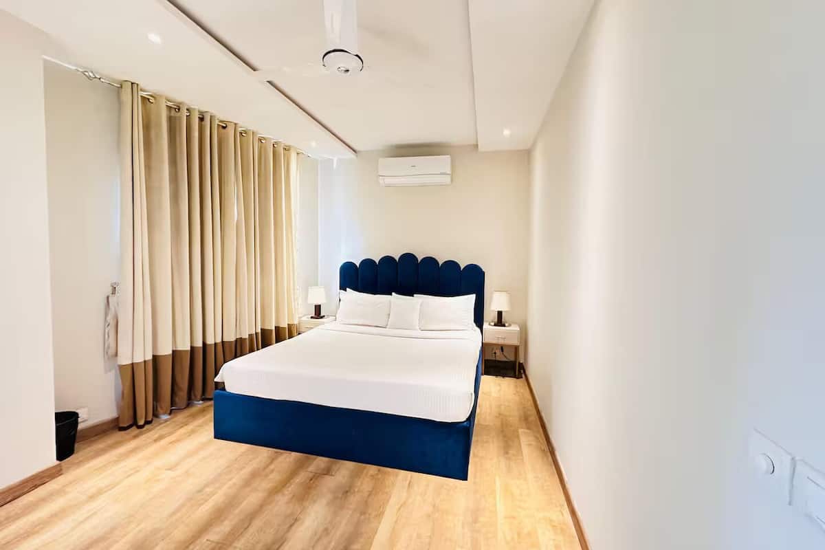 Une chambre d’hôtel moderne avec un grand lit, une tête de lit, des tables de chevet et une fenêtre avec des rideaux.