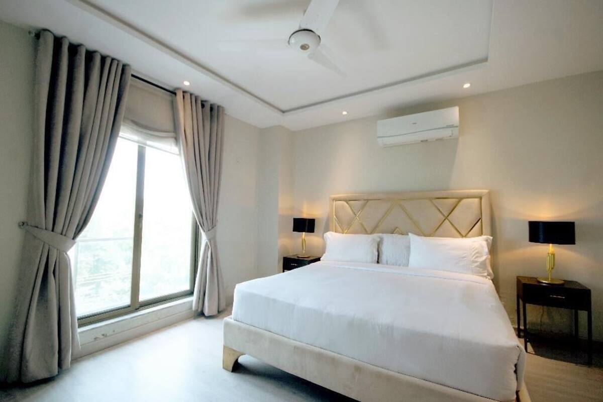 Une chambre d’hôtel avec un grand lit, deux tables de chevet, un ventilateur de plafond et une fenêtre avec des rideaux.