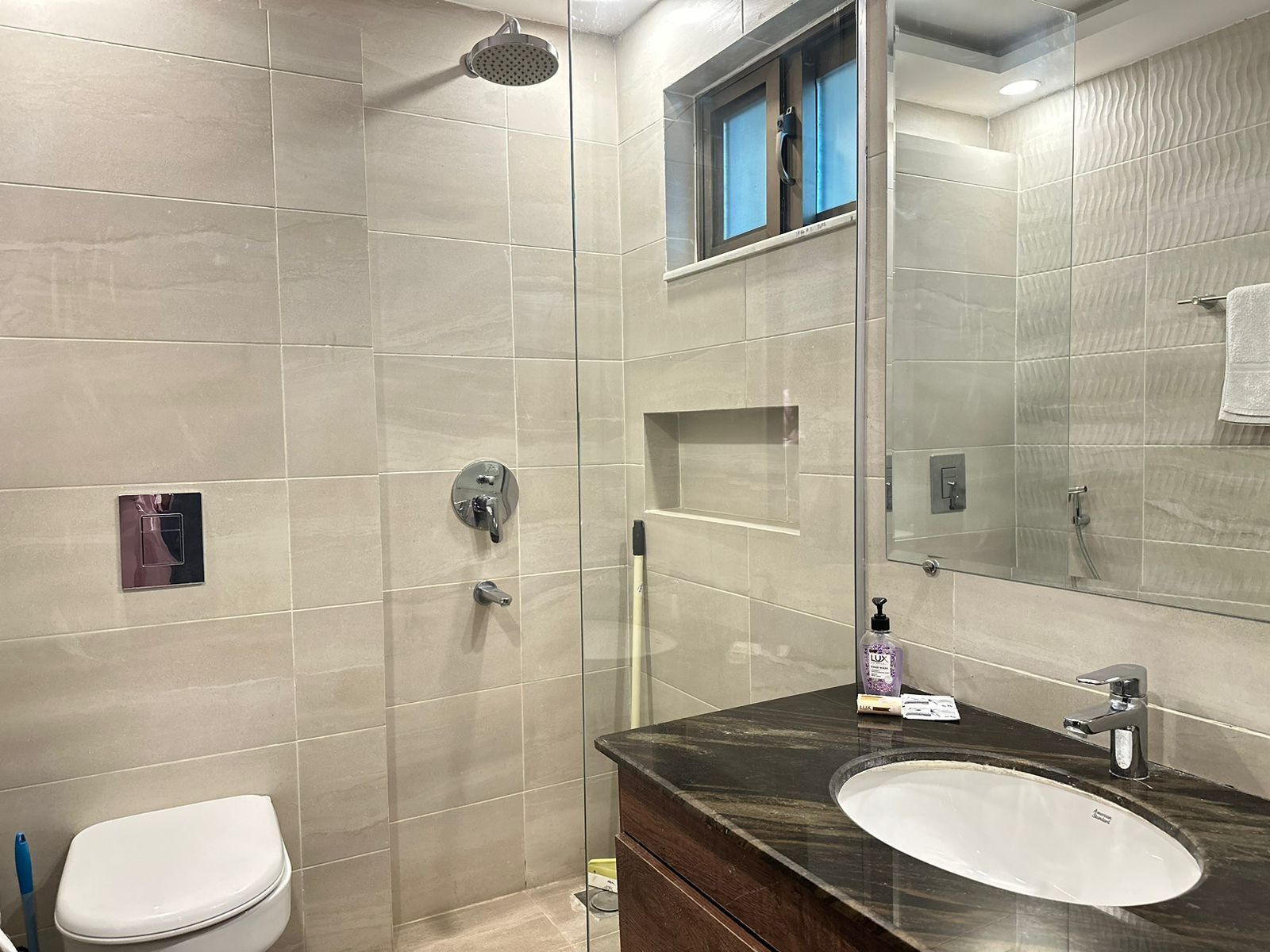 A modern bathroom with a glass-enclosed shower, a white toilet, and a dark marble sink with a mirror above it.