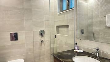 A modern bathroom with a glass-enclosed shower, a white toilet, and a dark marble sink with a mirror above it.