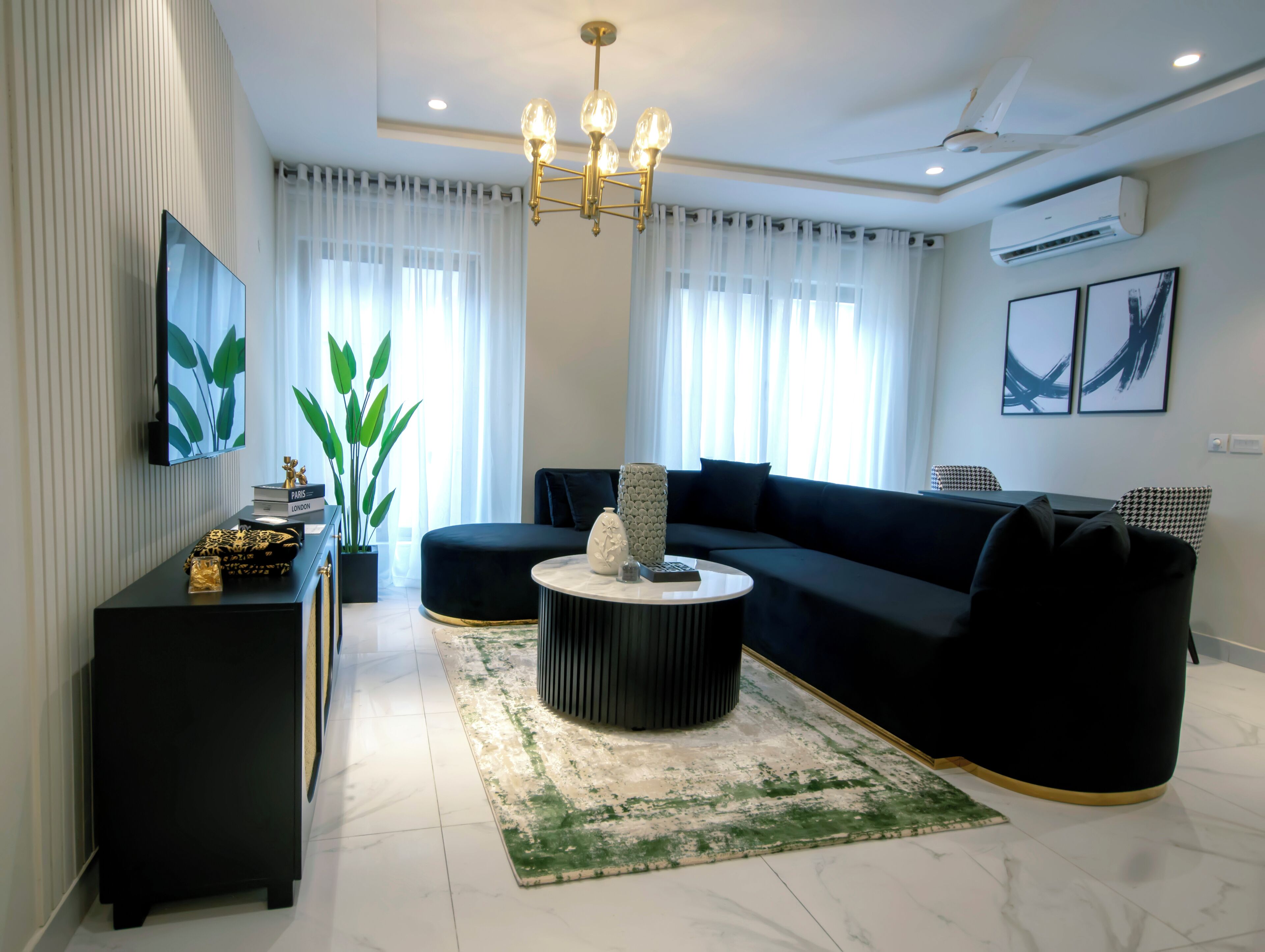 Una sala de estar moderna con un sofá negro, una mesa de centro redonda y un televisor montado en la pared.