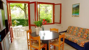 A dining area with a round table, chairs, a vase with flowers, and a sofa. - Charming family villa in Lignano (Lignano Sabbiadoro)