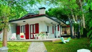 A house with a covered porch, a brick wall, and a lawn. - Charming family villa in Lignano (Lignano Sabbiadoro)