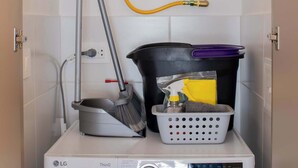 Un lavadero pequeño con una lavadora LG ThinQ de carga frontal, una manguera para el suministro de agua y un calentador de agua instalado en la pared.