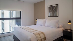 Una habitación de hotel moderna con una cama grande, una mesita de noche con lámpara y una obra de arte enmarcada en la pared.