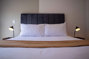 Restful retreat with a dark headboard and crisp white bedding, complemented by bedside lamps and a cozy throw blanket.