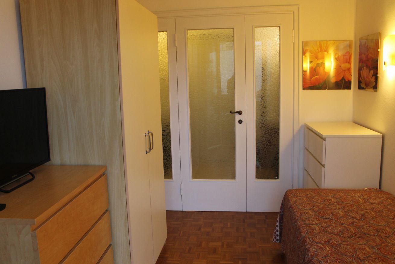 Una camera da letto con un letto, una TV su una cassettiera in legno, un armadio e una porta con vetri satinati.