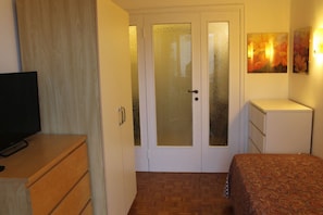 A bedroom with a bed, a TV on a wooden dresser, a wardrobe, and a door with frosted glass panels. - Coroneo33, spacious for families (Trieste)