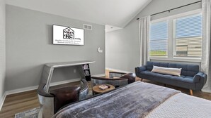 A modern bedroom with a bed, a desk, a sofa, and a window with blinds.
