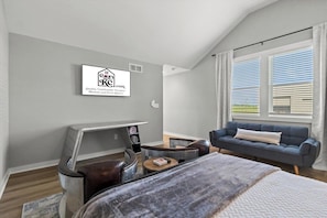 A modern bedroom with a bed, a desk, a sofa, and a window with blinds.