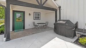 A covered patio with a grill, a green door, and a small table with chairs. - Pilot's Pad Studio on 75 Acres + Fishing Pond (Pleasant Hill)