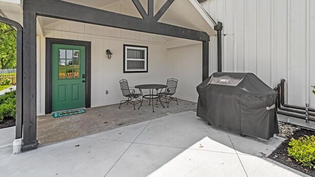 A covered patio with a grill, a green door, and a small table with chairs.