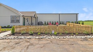 A building with a garage, a fenced patio area with outdoor seating, and a gravel driveway. - Pilot's Pad Studio on 75 Acres + Fishing Pond (Pleasant Hill)