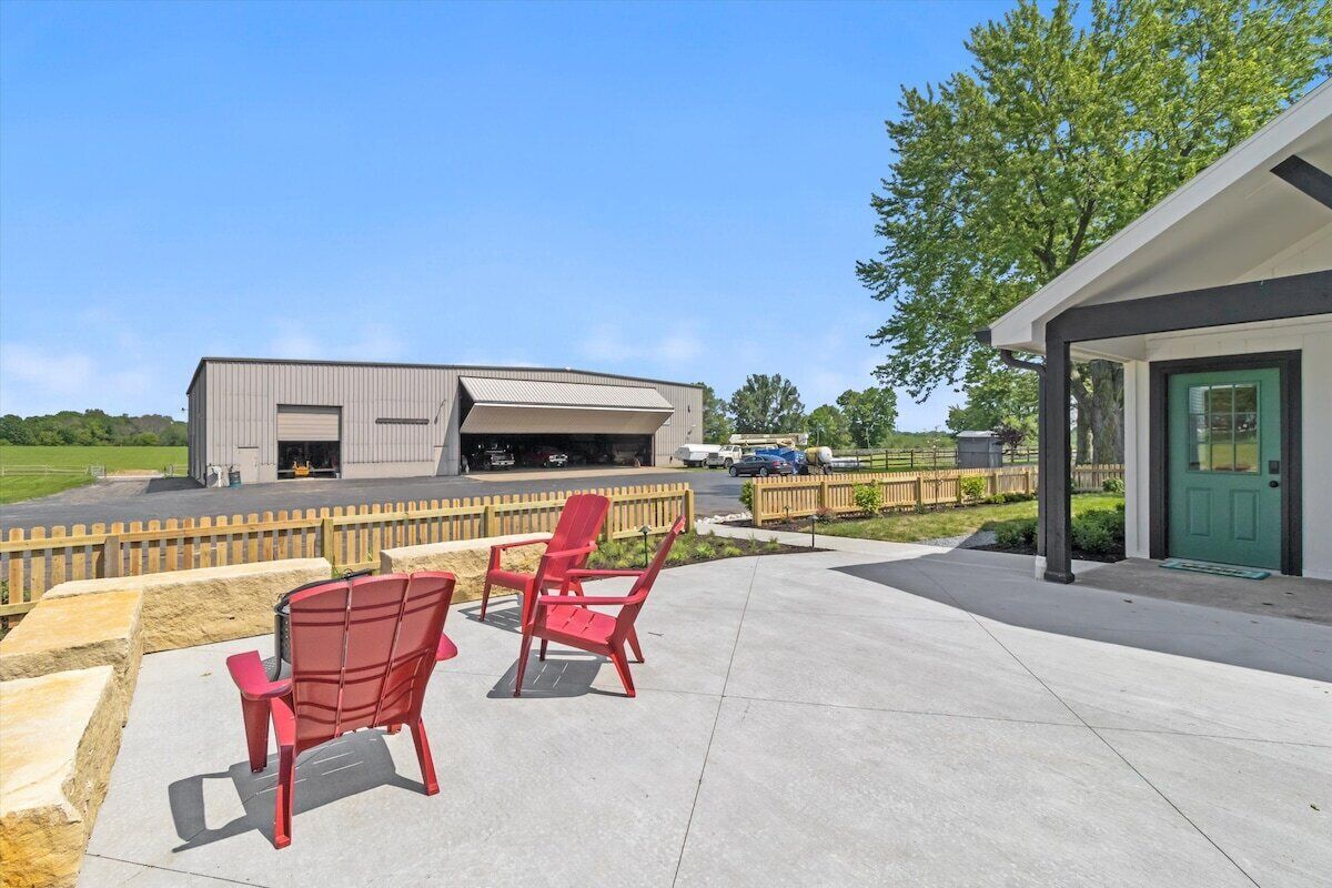 A building with a large garage door, outdoor seating with red chairs, and a green door.