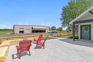A building with a large garage door, outdoor seating with red chairs, and a green door.
