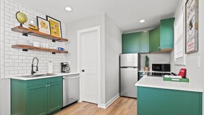 A compact kitchen with green cabinets, a white countertop, and a wooden floor.