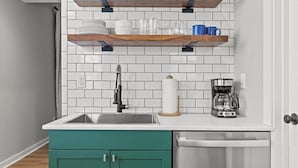 A kitchen with a white tiled backsplash, a stainless steel sink, a coffee maker, and teal cabinets.