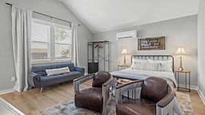 A bedroom with a bed, two bedside tables, a nightstand, a window with blinds, a sofa, and two chairs. - Pilot's Pad Studio on 75 Acres + Fishing Pond (Pleasant Hill)