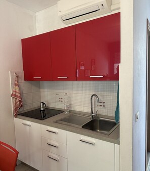 A compact kitchen with red cabinets, a stainless steel sink, and a tiled backsplash.