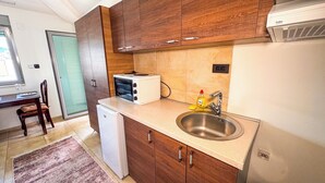 A compact kitchen with wooden cabinets, a built-in oven, a sink, and a small refrigerator. - Qumi Apartments (Tivat)