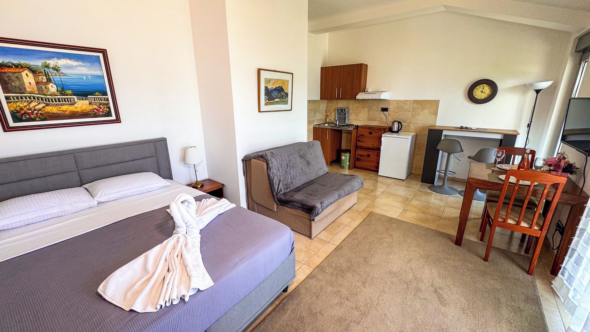A compact hotel room with a bed, a sofa, a small kitchenette, and a dining area.