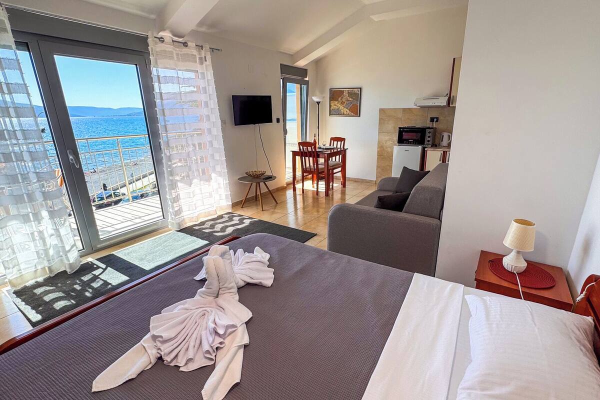A hotel room with a bed, a sofa, a dining area, and a view of the sea.