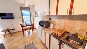 A compact kitchen with a dining area, a TV mounted on the wall, and a view through the door. - Qumi Apartments (Tivat)