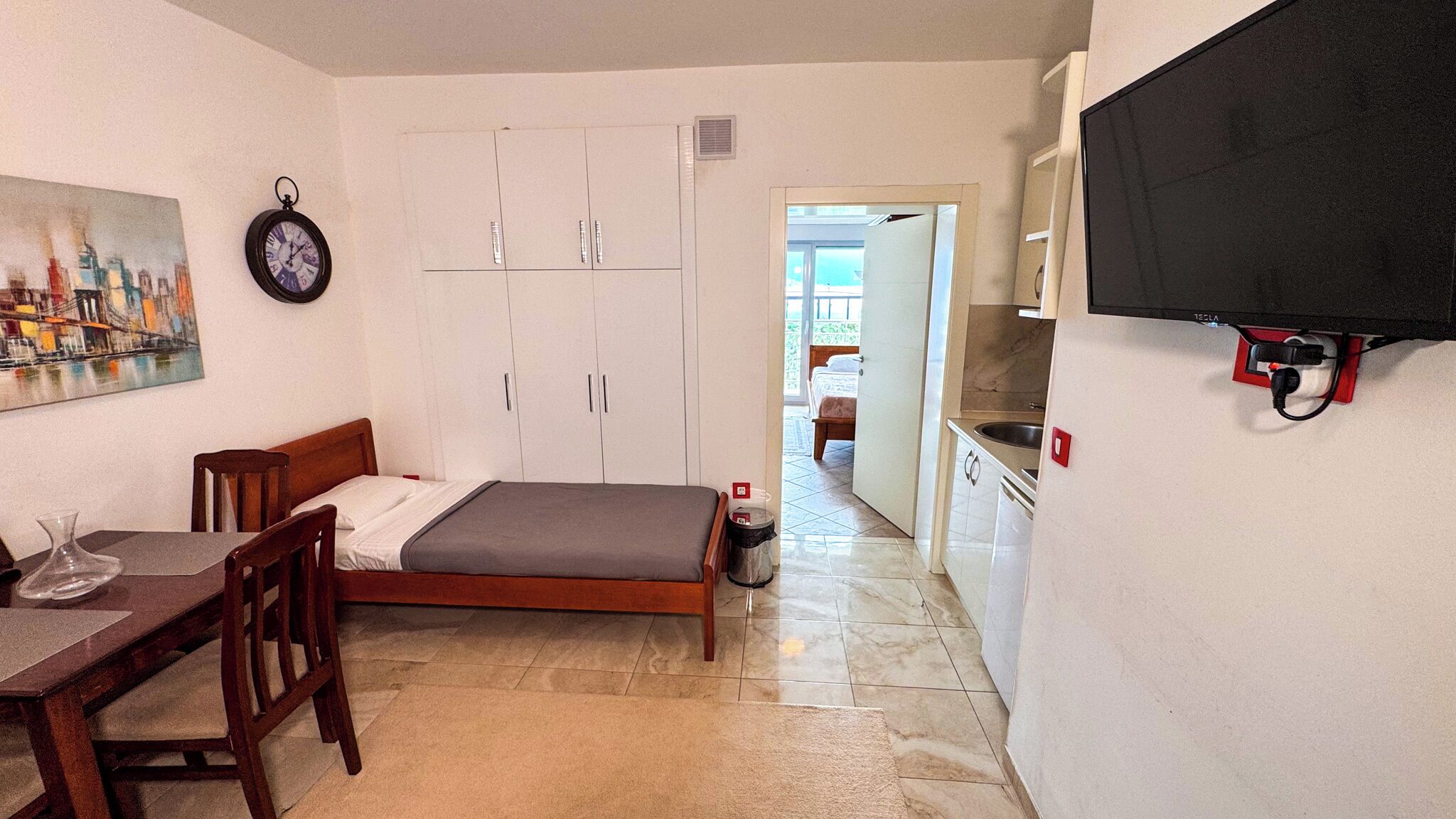 Ein gemütlicher Raum mit Bett, Esstisch, an der Wand montiertem Fernseher und einer Küchenzeile.