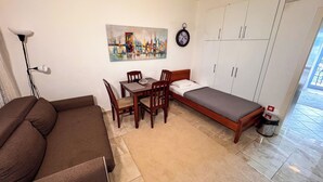 A compact room with a bed, a desk with chairs, a painting, and a clock on the wall. - Qumi Apartments (Tivat)
