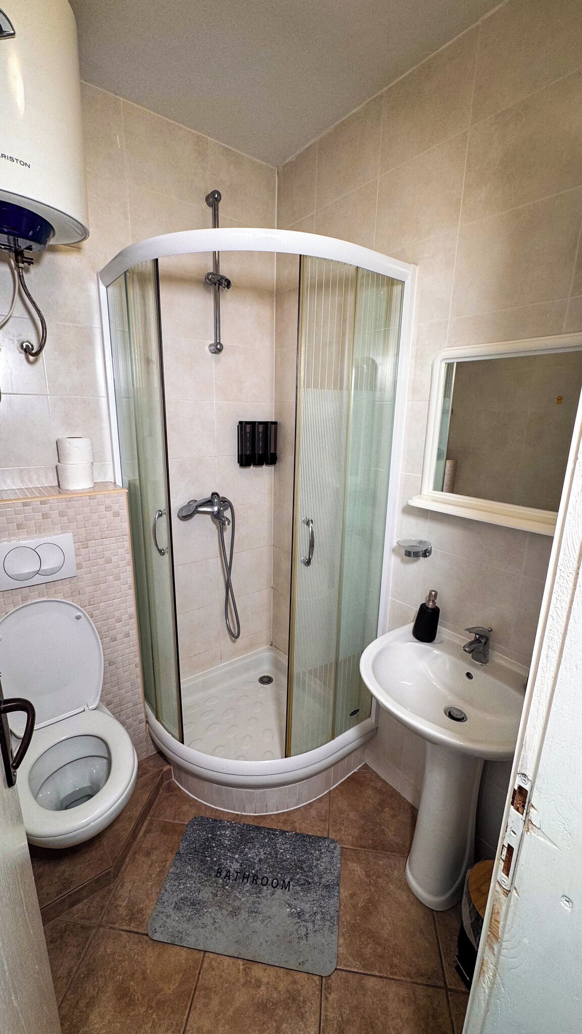 Een badkamer met een douche met glazen wand, een toilet, een wastafel en een spiegel.