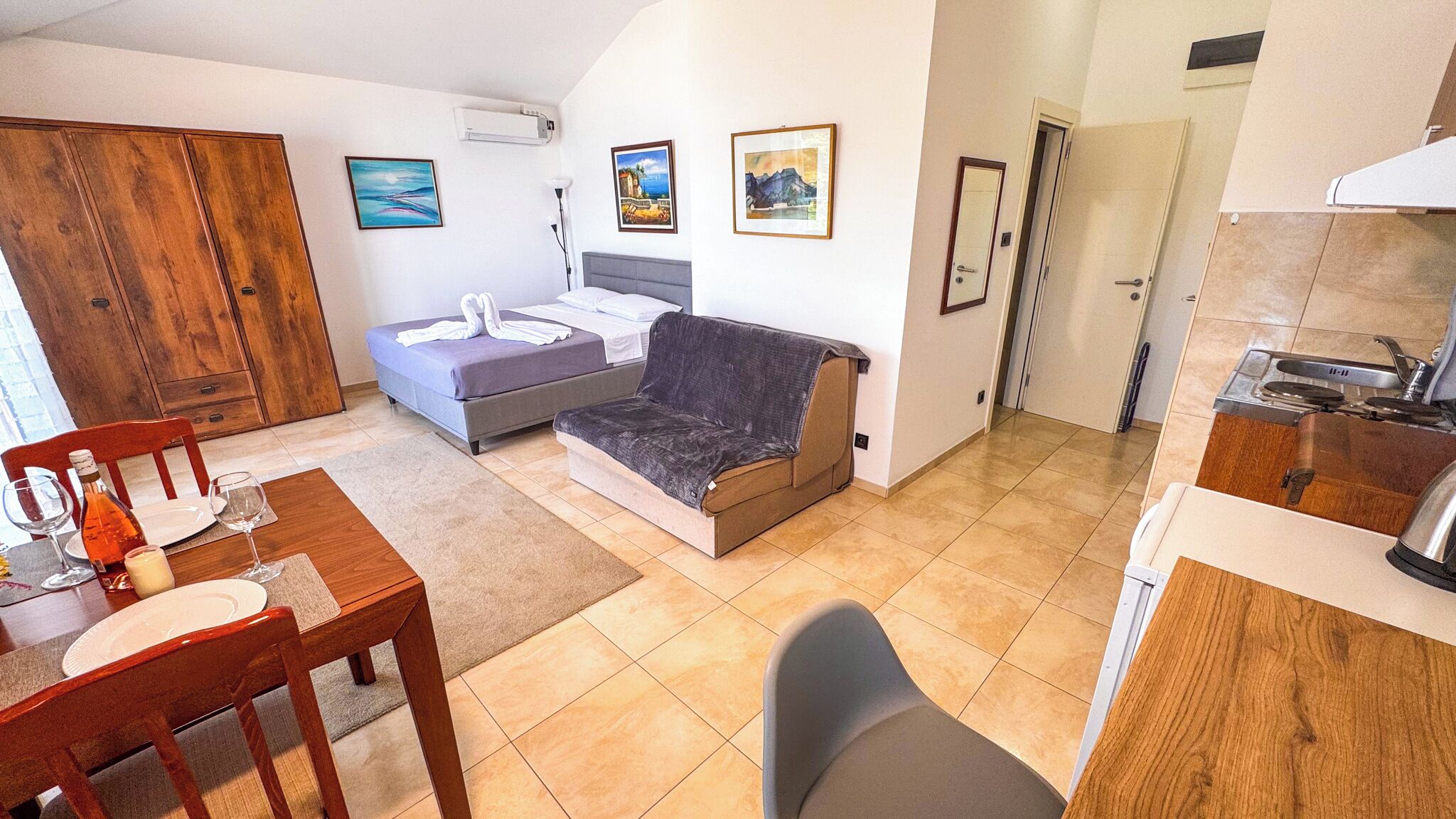 Une pièce de taille modeste comprenant un lit, un canapé, une table à manger avec des chaises, un coin cuisine et une armoire en bois.