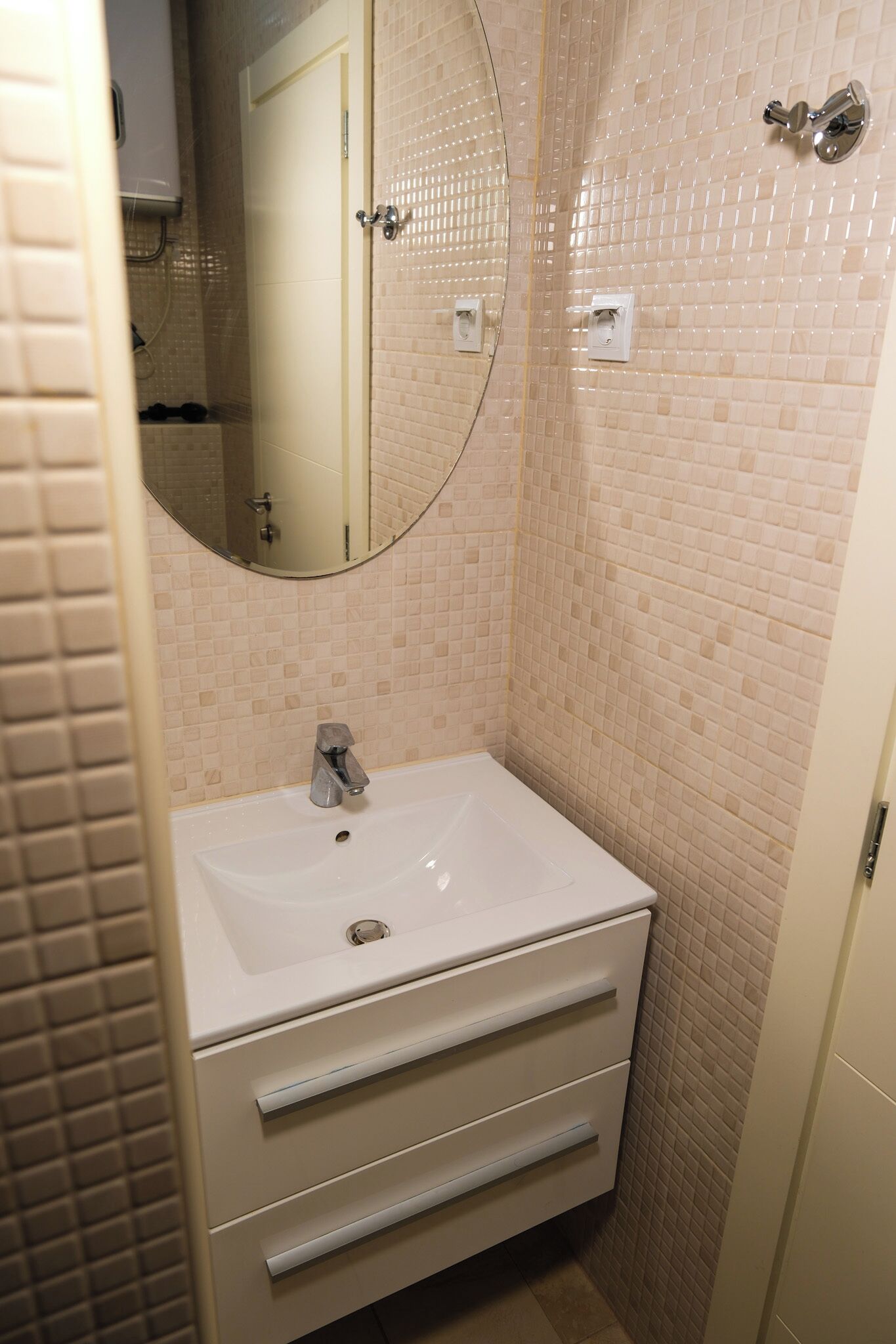 A bathroom with a white sink, a mirror, and a tiled wall.