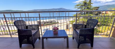 Un balcón con dos sillones de mimbre y una pequeña mesa, con vistas a una playa y montañas.