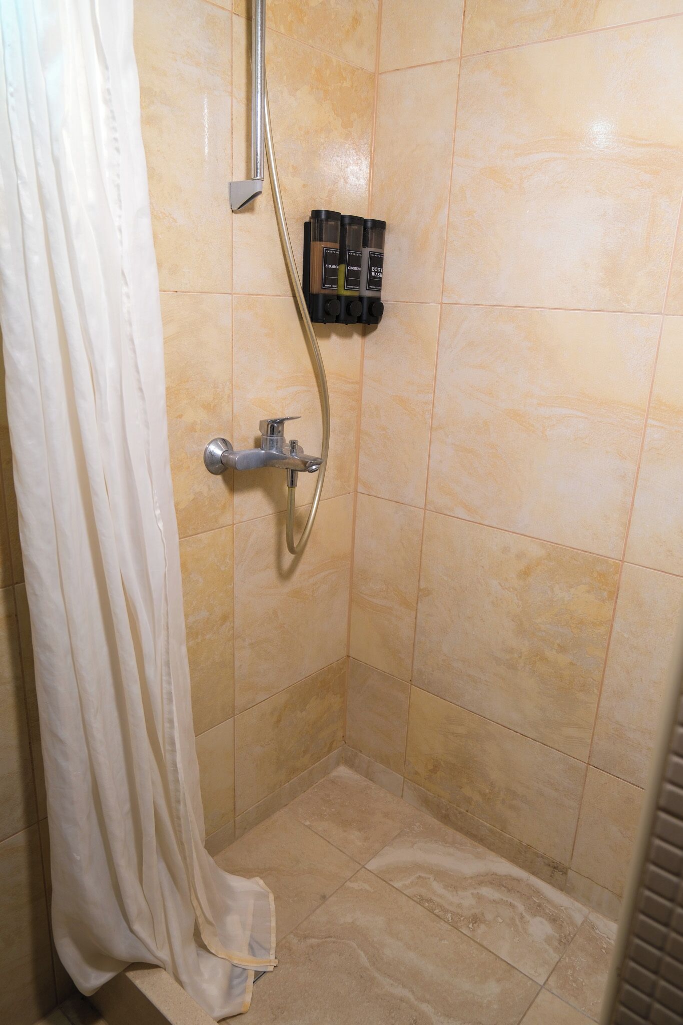 Eine Dusche mit Handbrause, einer fest installierten Bedienung und einem weißen Duschvorhang.