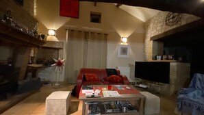 Een gezellige woonkamer met een open haard, een rode bank, een salontafel met boeken en een televisie.
