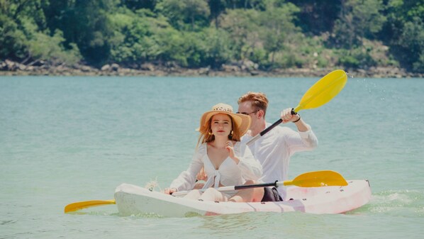 Una pareja en kayak sobre aguas tranquilas, con una orilla boscosa al fondo.