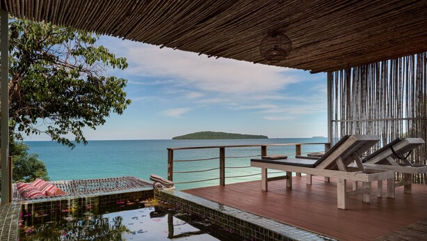 Una terraza de madera con piscina, sillas de descanso y vista al mar.