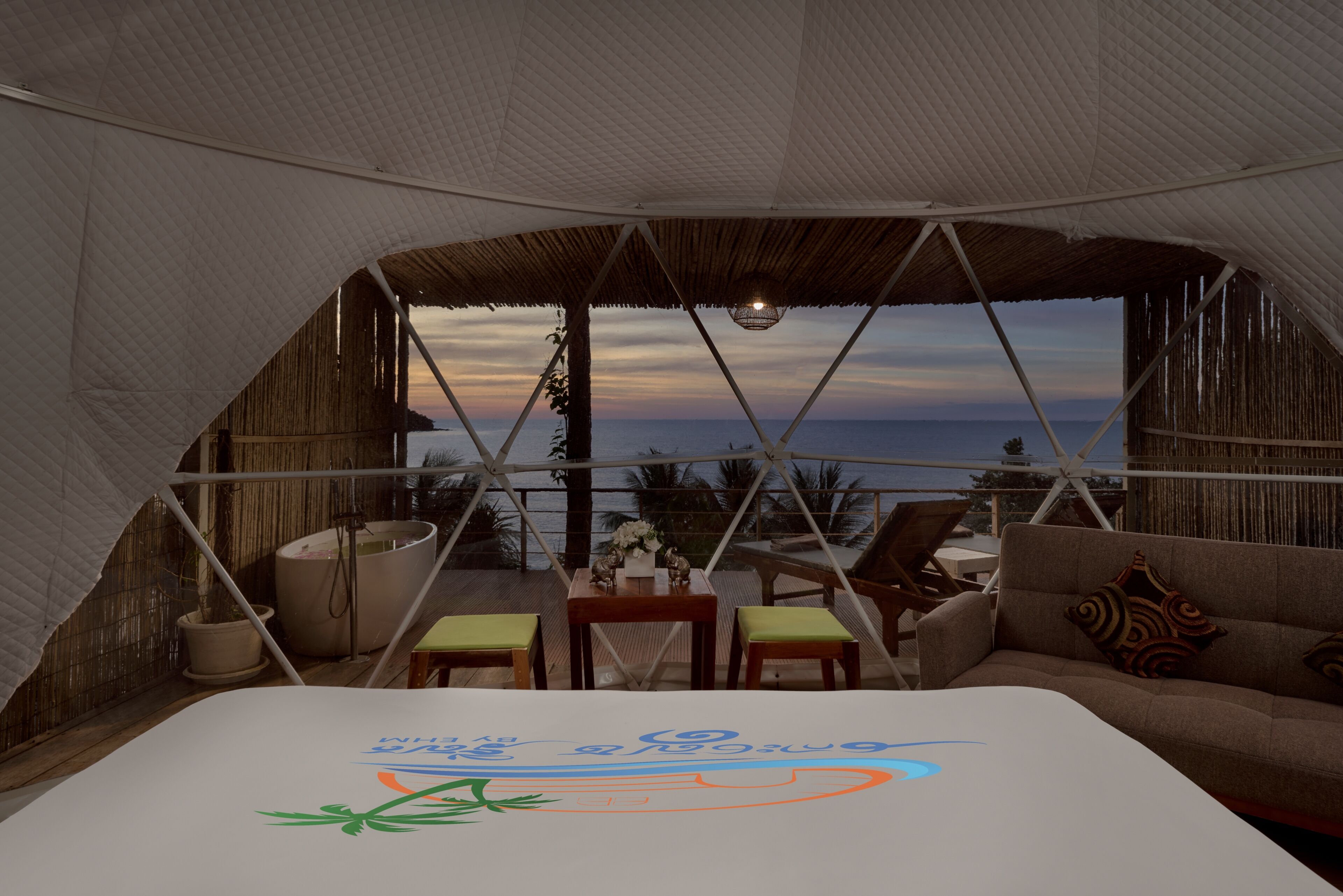 Alojamiento en tienda de campaña con cama, zona de estar y vista al mar.