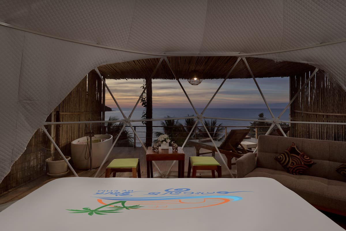 Alojamiento en tienda de campaña con cama, zona de estar y vista al mar.
