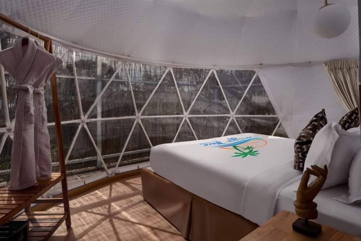 Una habitación acogedora con una cama, un banco de madera y un ventanal con vistas a árboles.