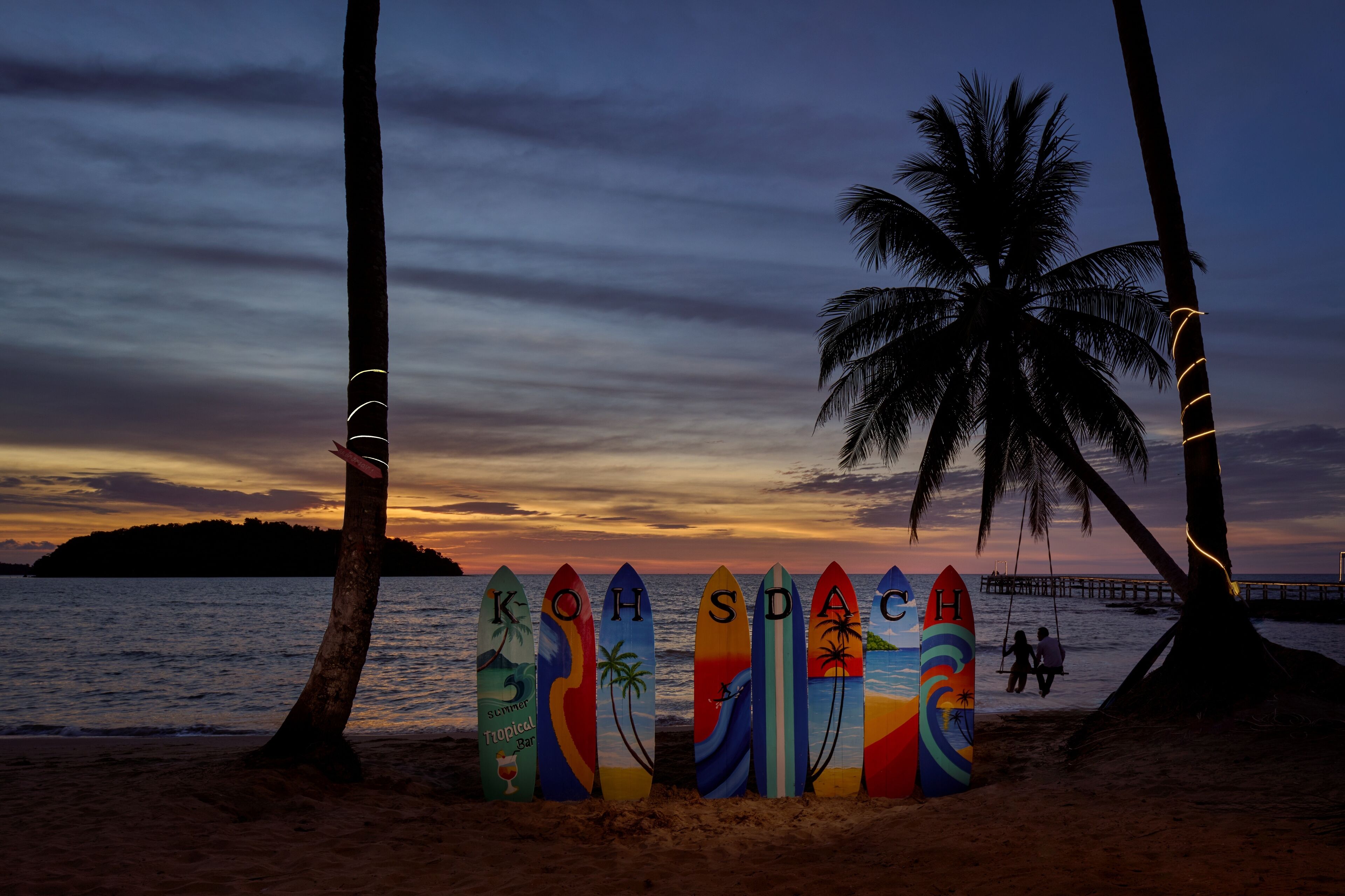 Uma praia com pranchas de surf alinhadas e palmeiras.