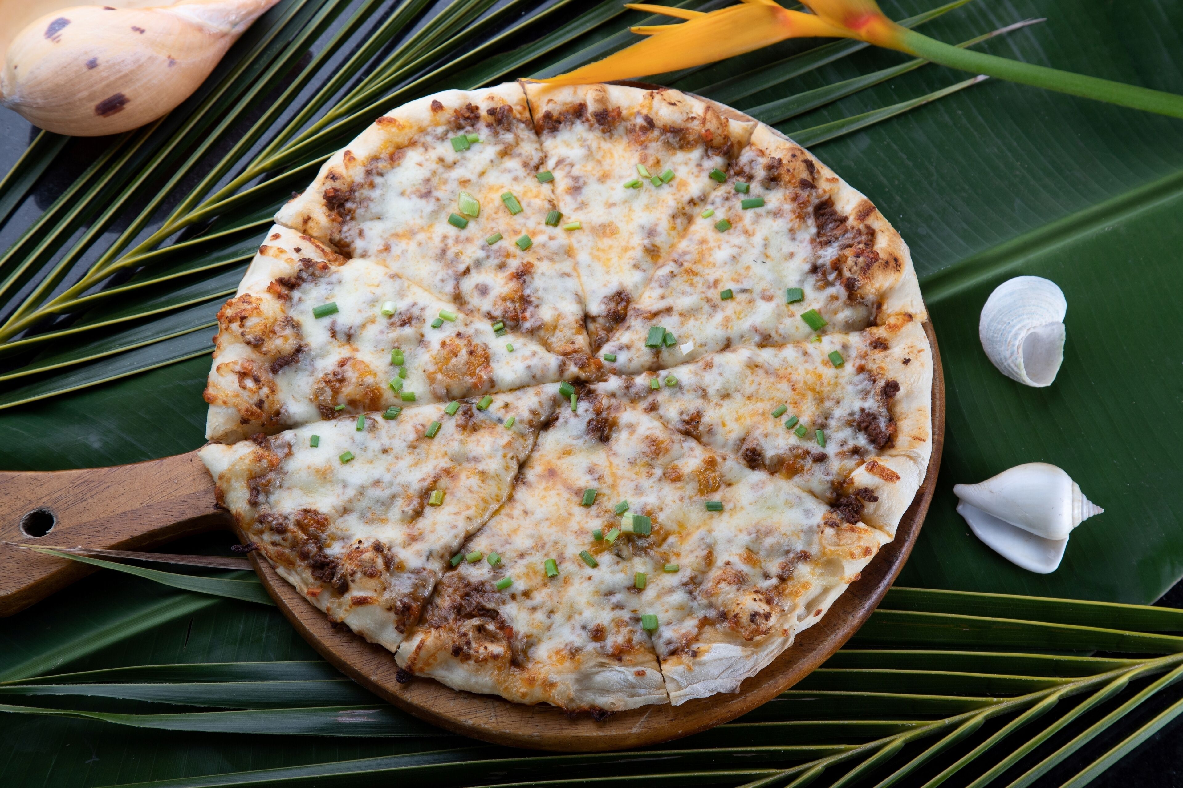Uma pizza sobre uma tábua de madeira, com uma banana e uma concha ao fundo.