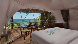 Alojamiento en tienda de campaña con cama, mesa, sillas y vista al mar.