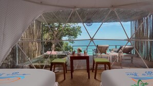 Habitación con tienda de campaña, dos camas, una mesa y sillas, con vista a una piscina y al mar.